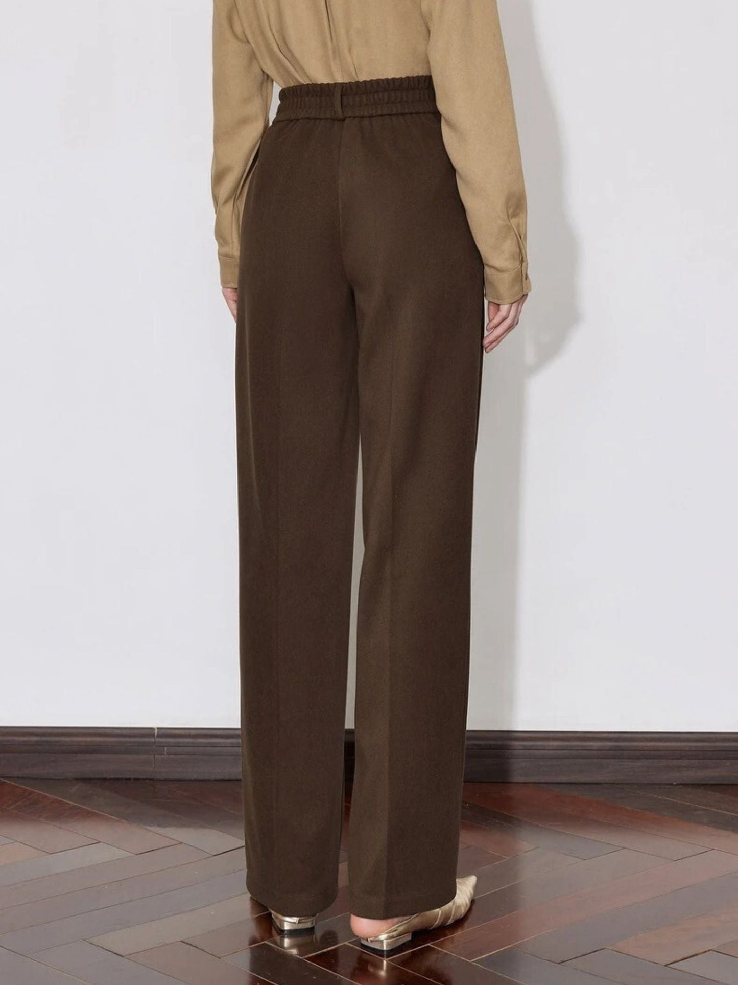 Back view of brown pants styled with a beige shirt and heeled loafers.