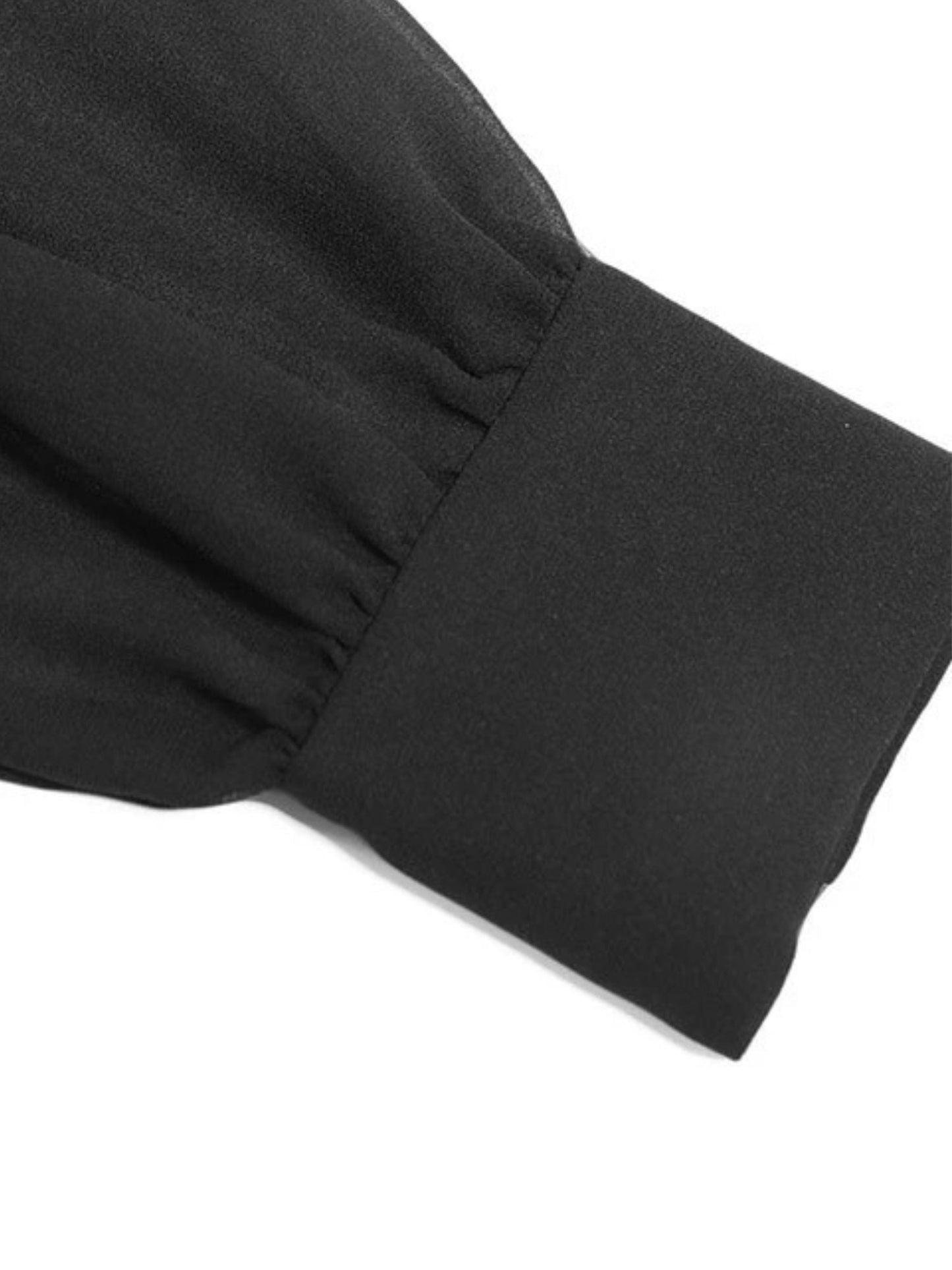 Detailed view of smocked cuff on sheer long sleeve of black dress.