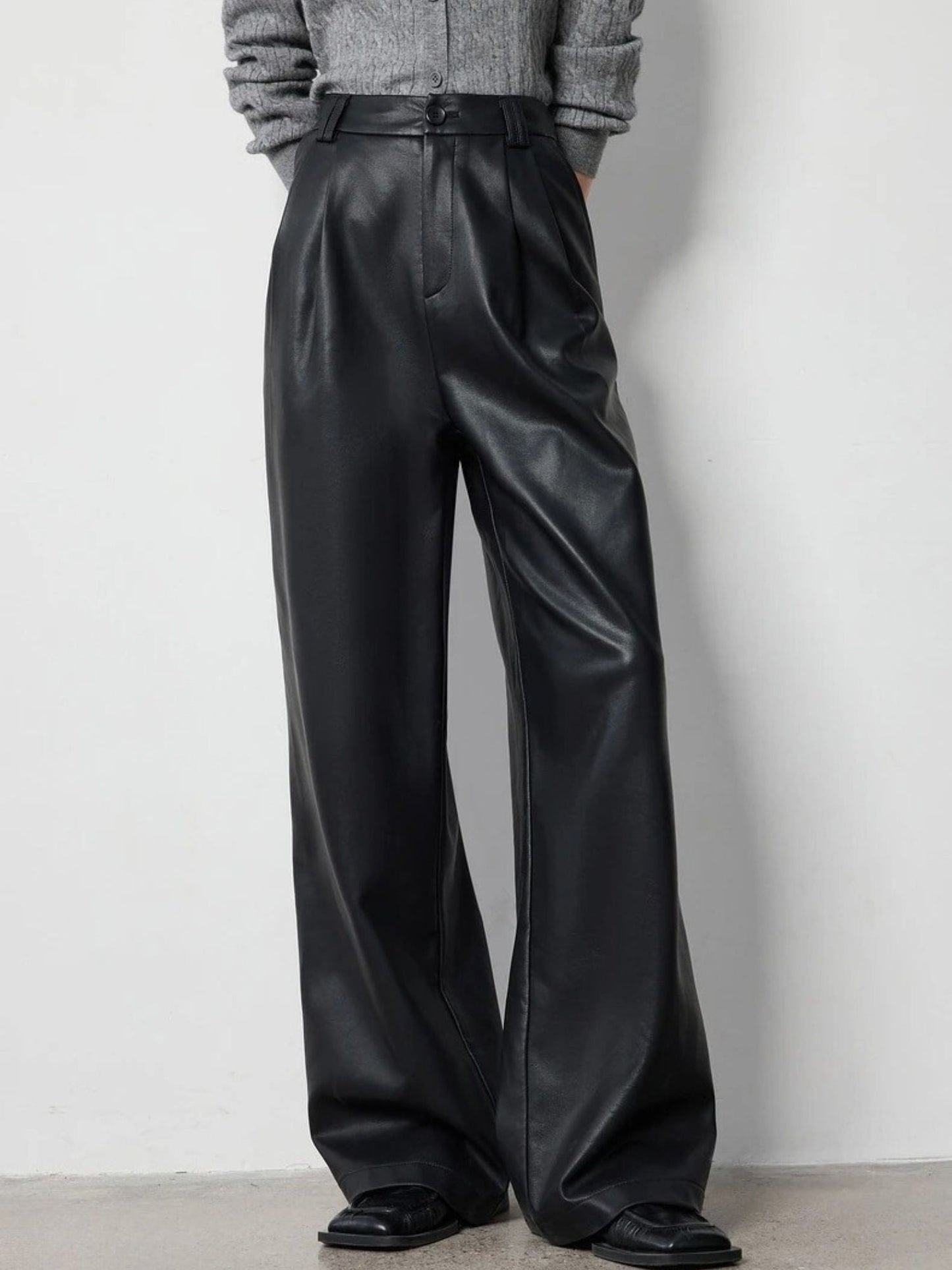 Waist-down view of black leather-look pants styled with a tucked grey sweater.