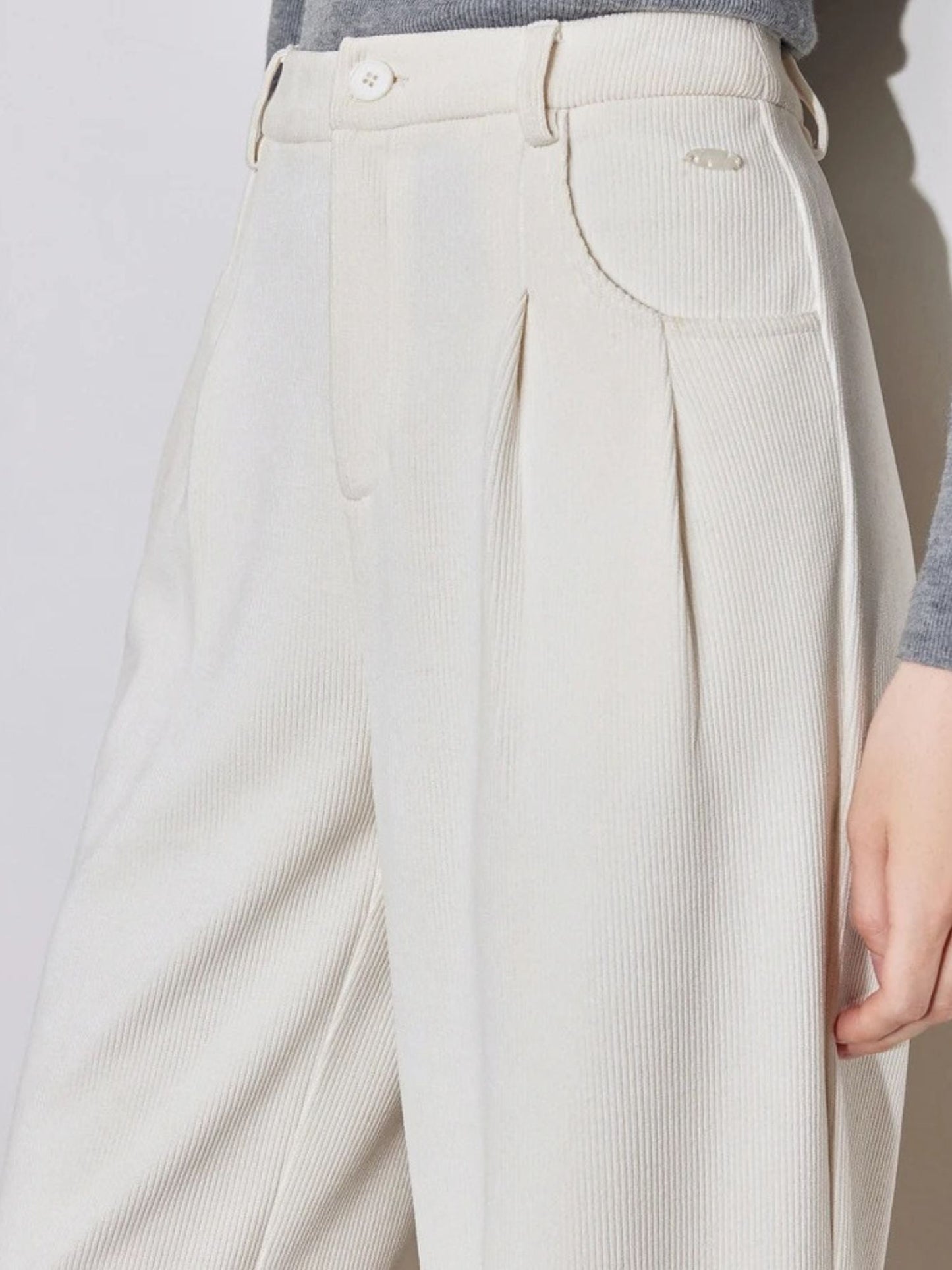 Close-up of cream wide-leg trousers with side pocket and belt loops.