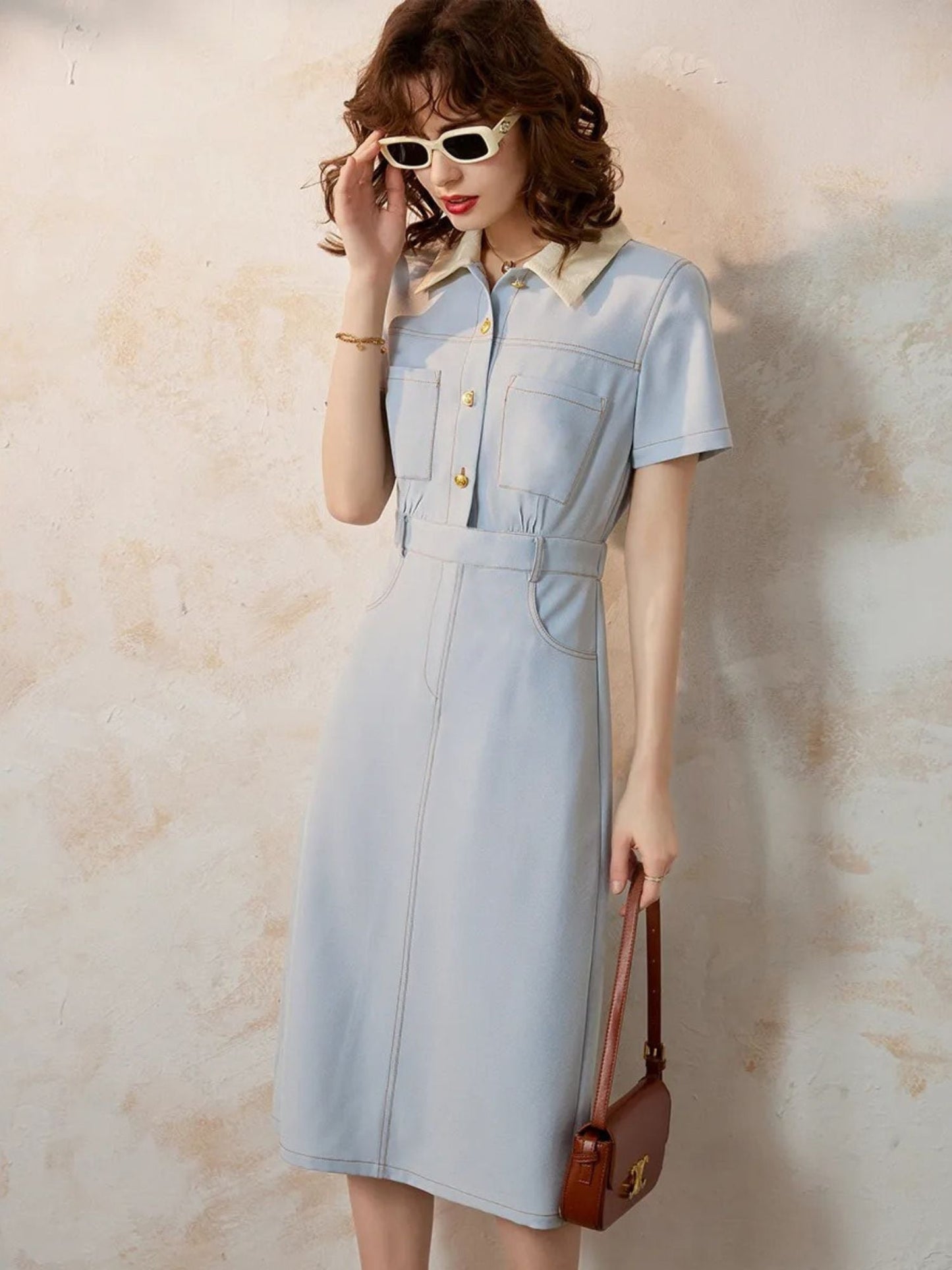 Side view of tailored blue dress styled with a brown shoulder bag.