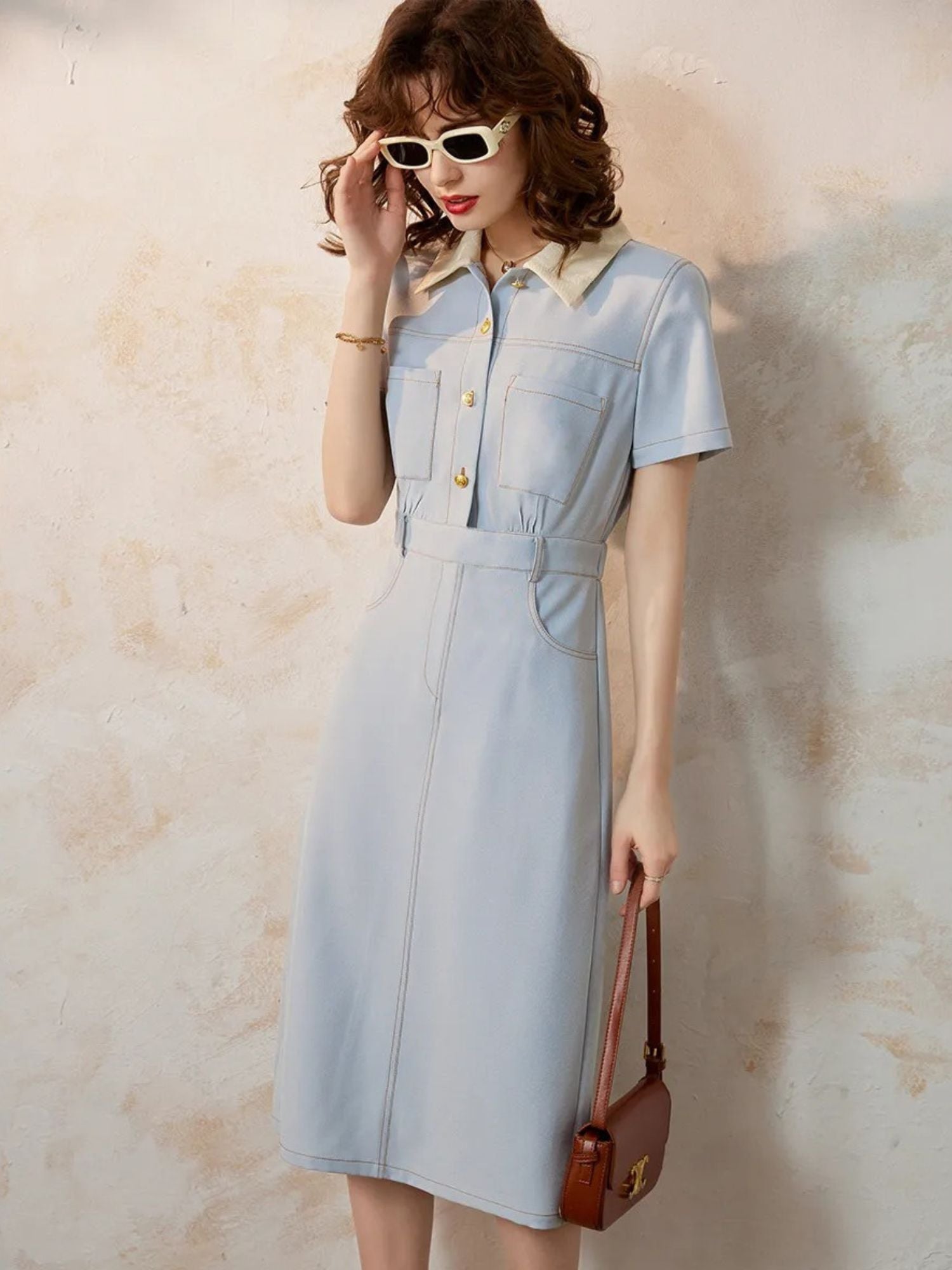 Side view of tailored blue dress styled with a brown shoulder bag.