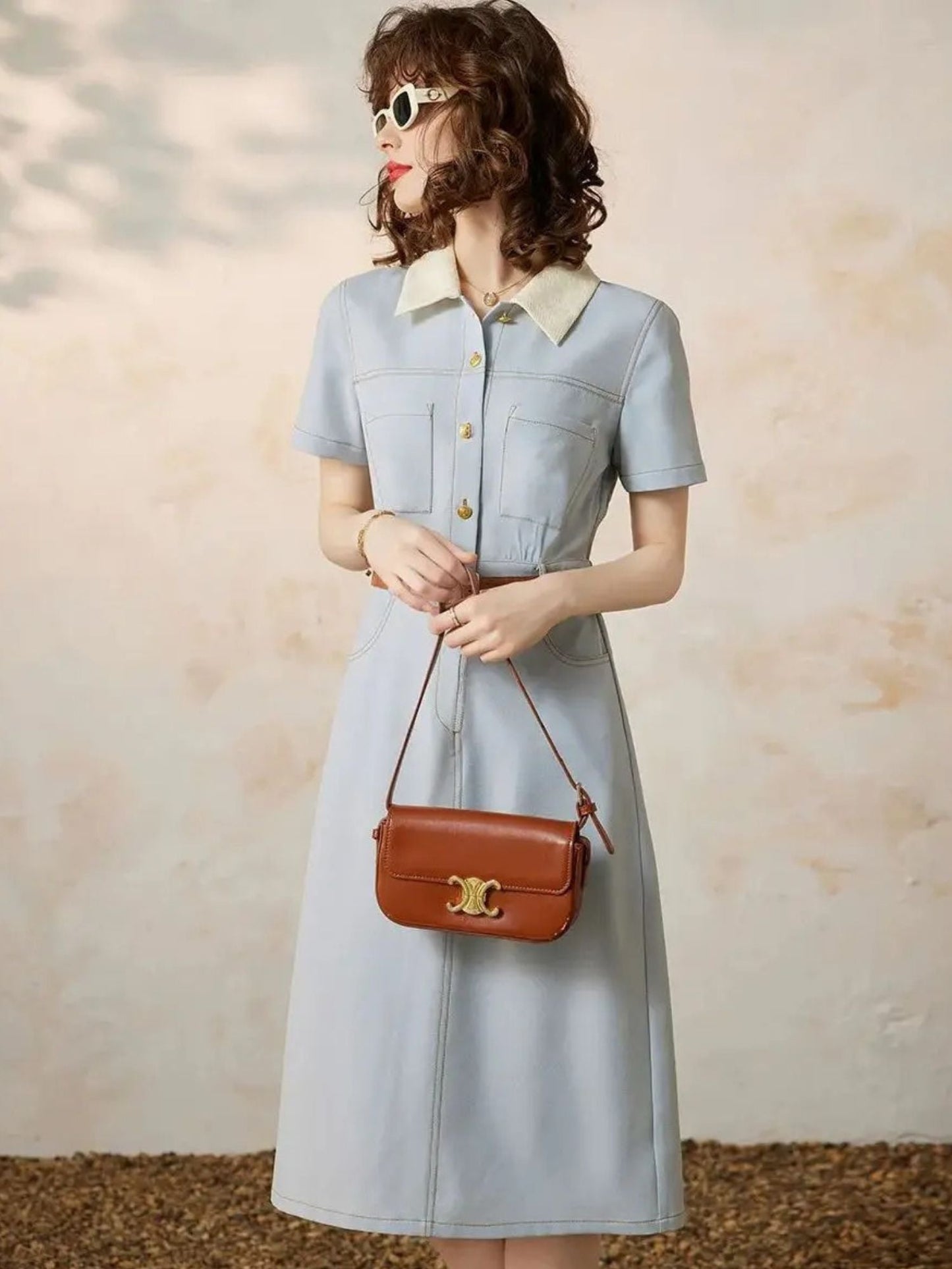 Angled view of light blue button-up dress with pleats and short sleeves.