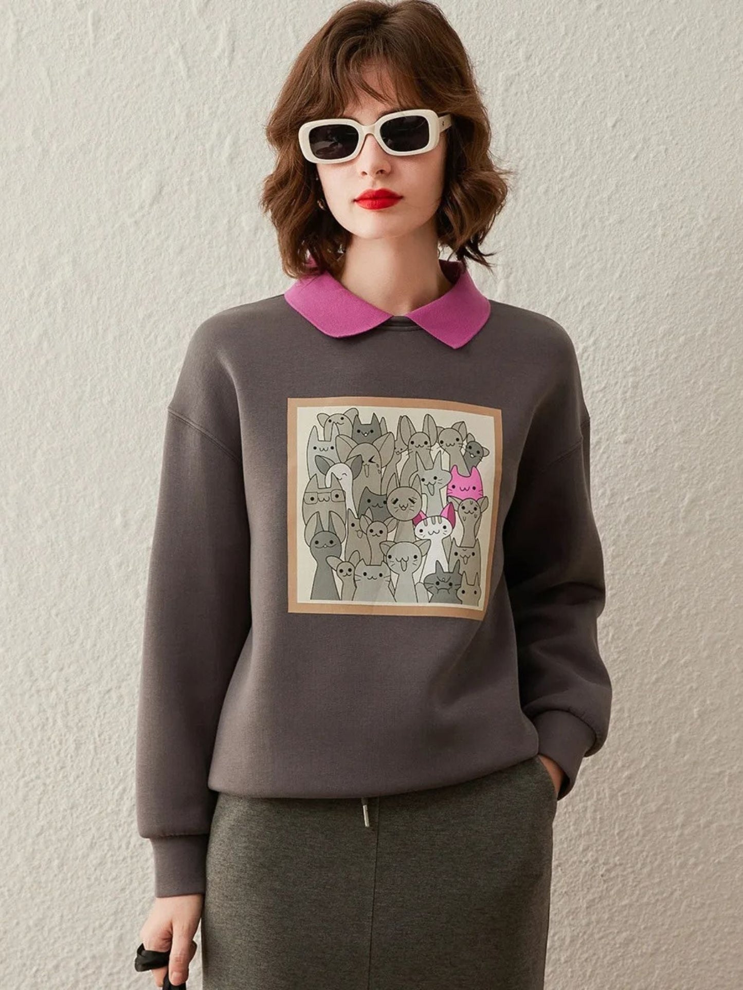 Model in dark grey sweatshirt with graphic print and bright pink collar, wearing sunglasses.