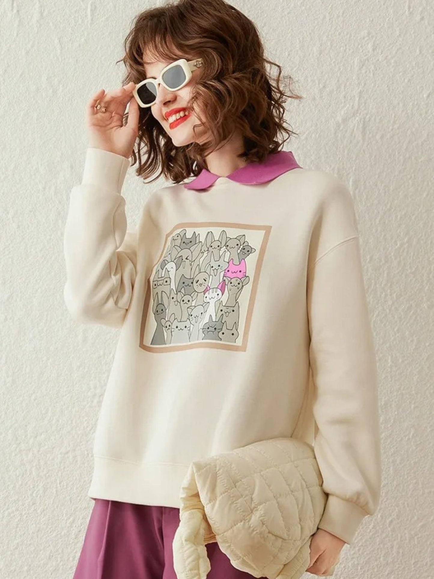 Cream graphic sweatshirt with white clutch, styled with sunglasses.