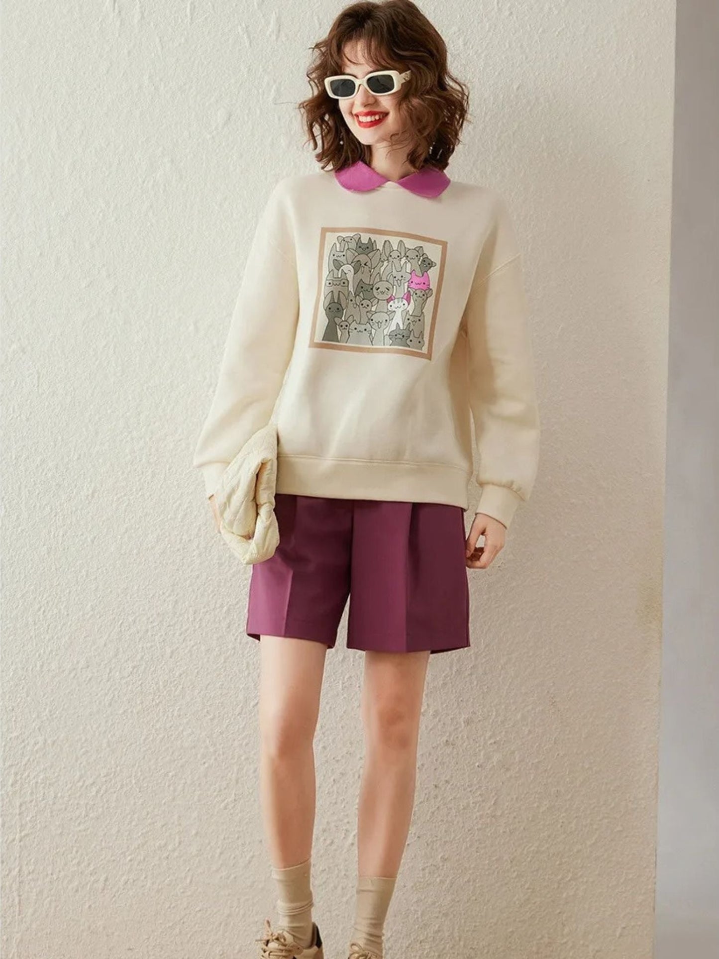 Model adjusting sunglasses in cream sweatshirt and pink collared shirt.