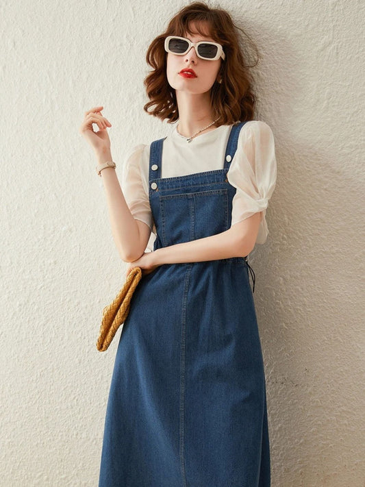 Model in denim pinafore dress with puff sleeve blouse, white sunglasses, and yellow clutch.