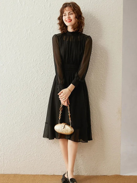 Model in long-sleeve black chiffon midi dress holding a pearl handle handbag.
