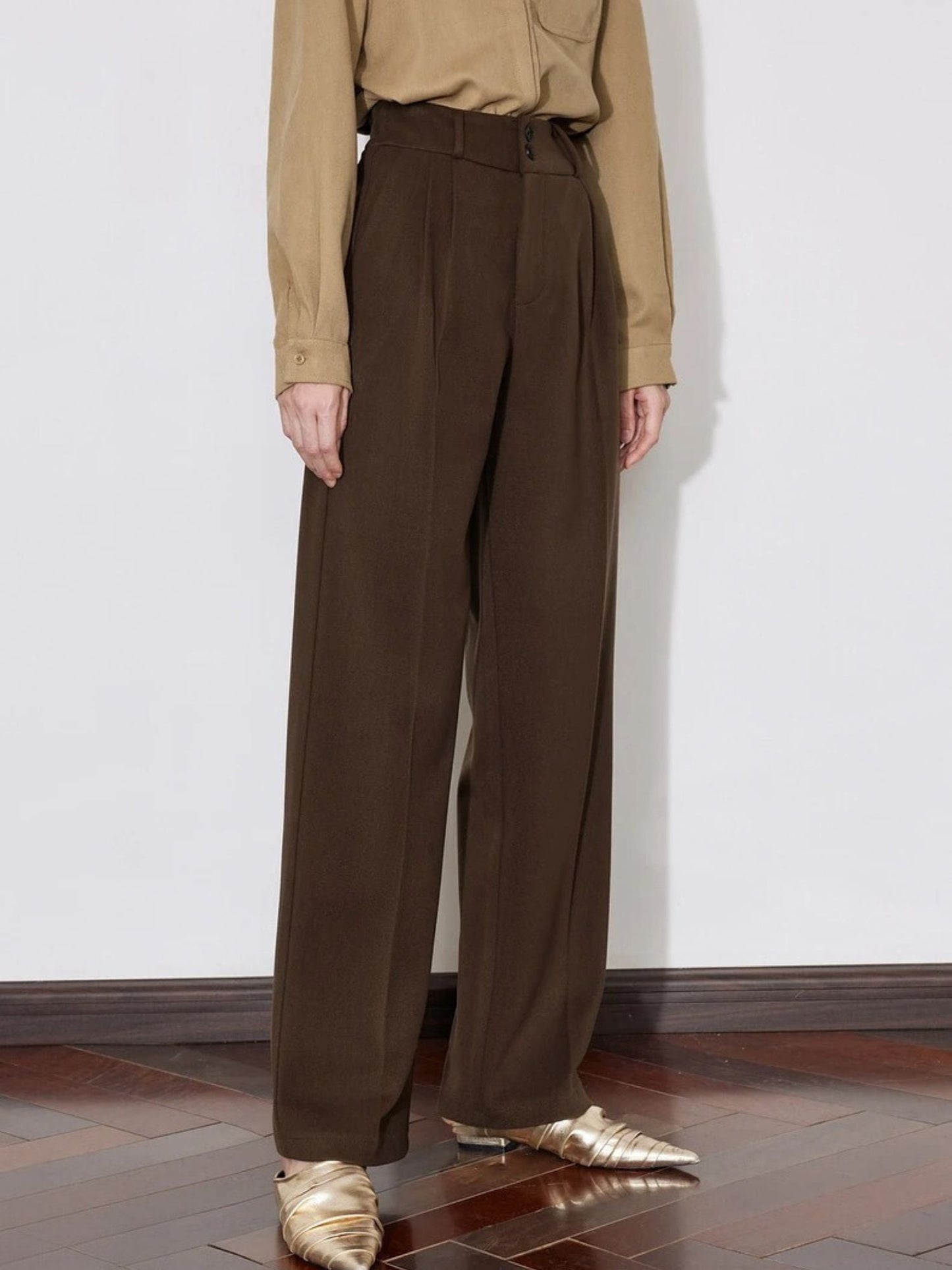 Side view of brown wide-leg pants with pressed crease and relaxed fit.