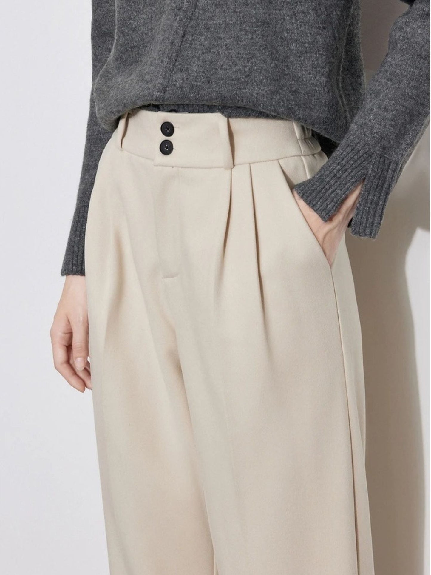 Close-up of beige high-waisted pants with pleats and waistband detail.