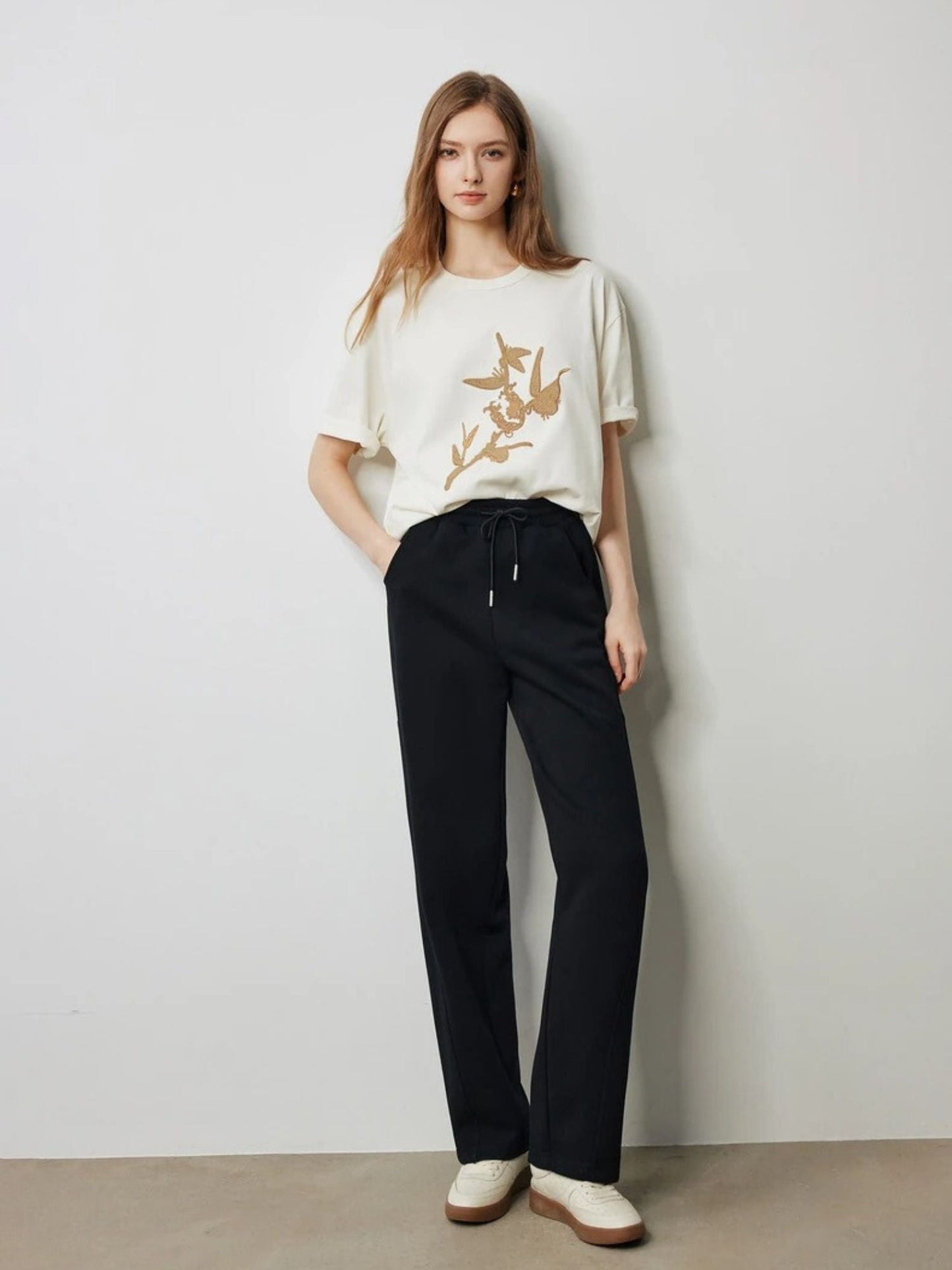 Model in black drawstring trousers with a cream graphic t-shirt and loafers.