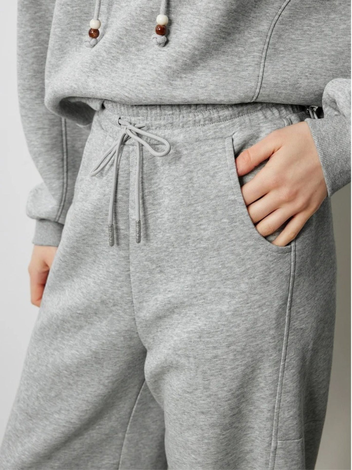 Close-up of grey drawstring pants with hand in pocket and textured knit fabric.