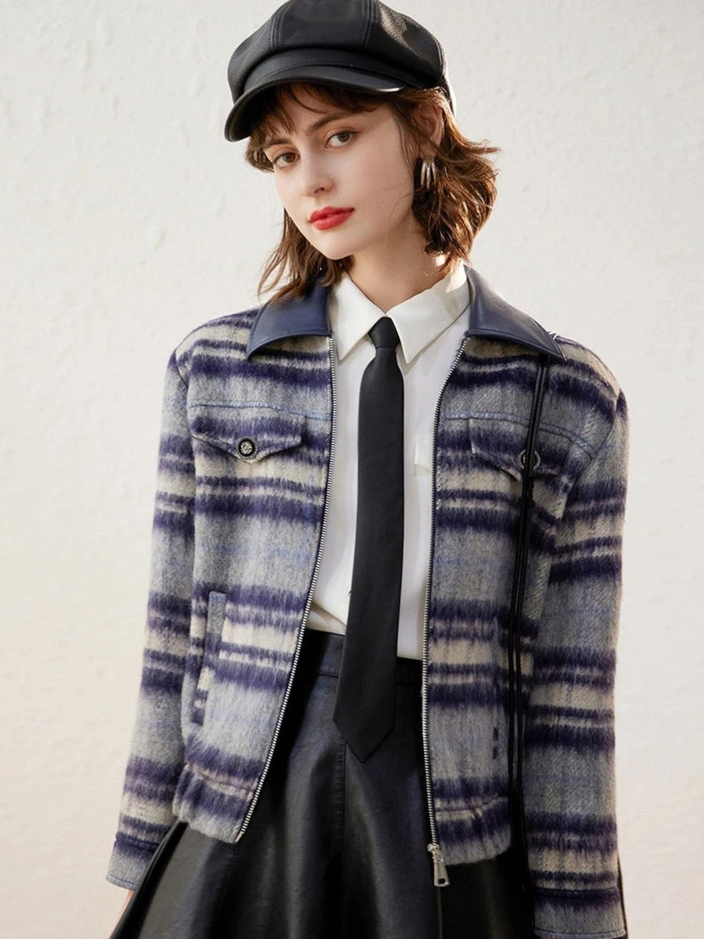 Model in a purple plaid zip-up jacket with white blouse and black skirt, wearing a newsboy cap.