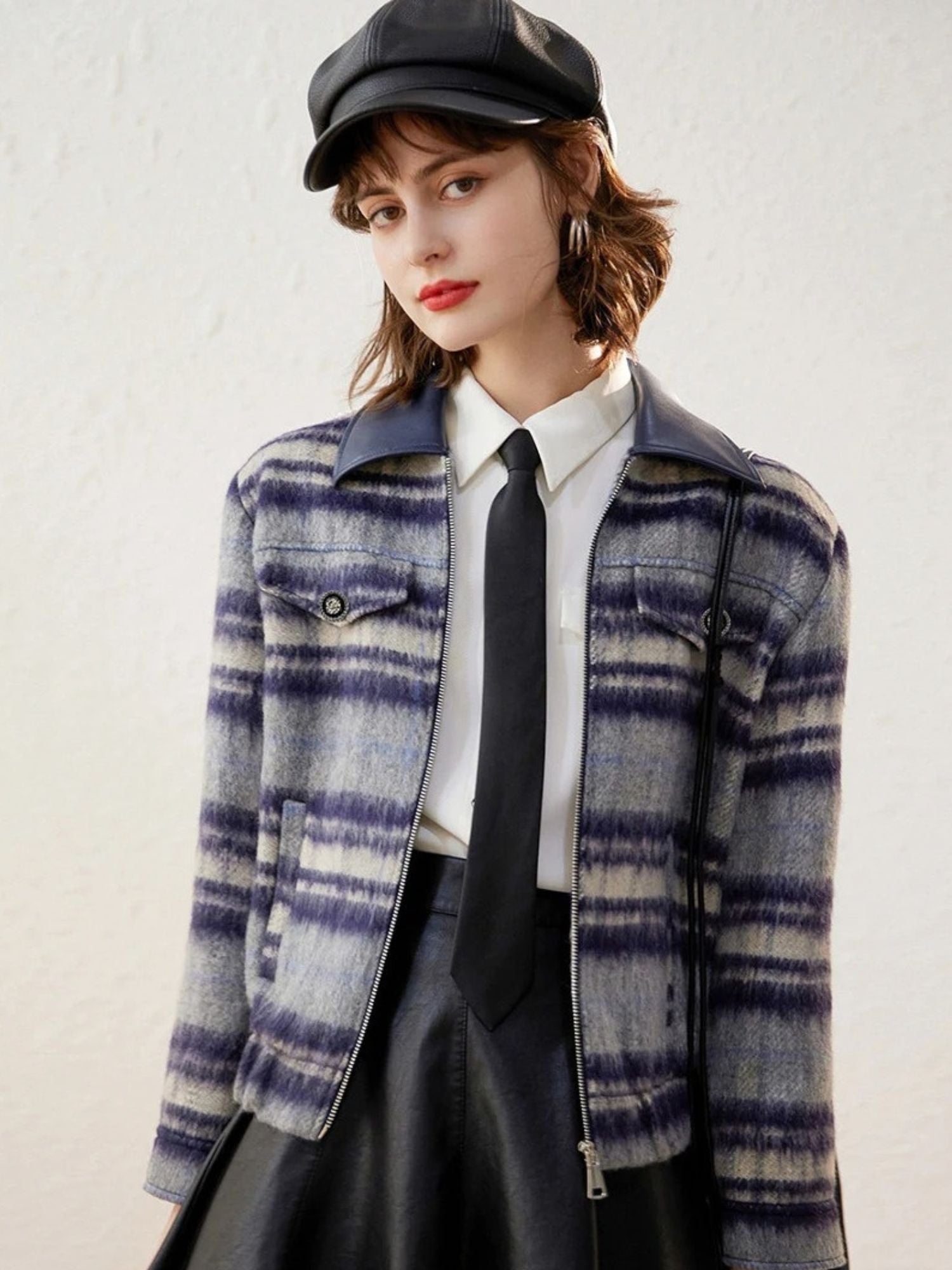 Model in a purple plaid zip-up jacket with white blouse and black skirt, wearing a newsboy cap.