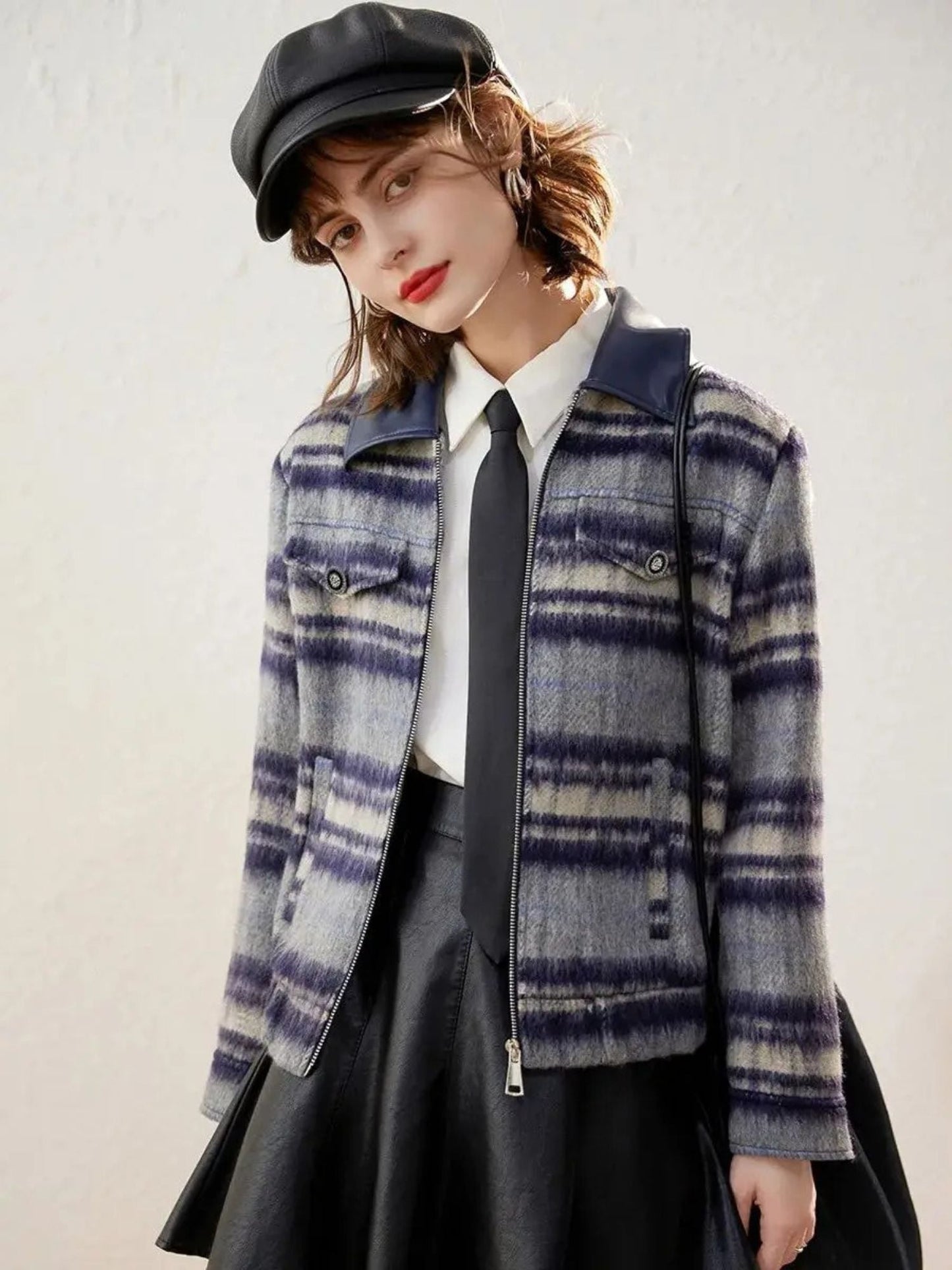 Model looking down in purple plaid jacket, styled with a black pleated skirt.