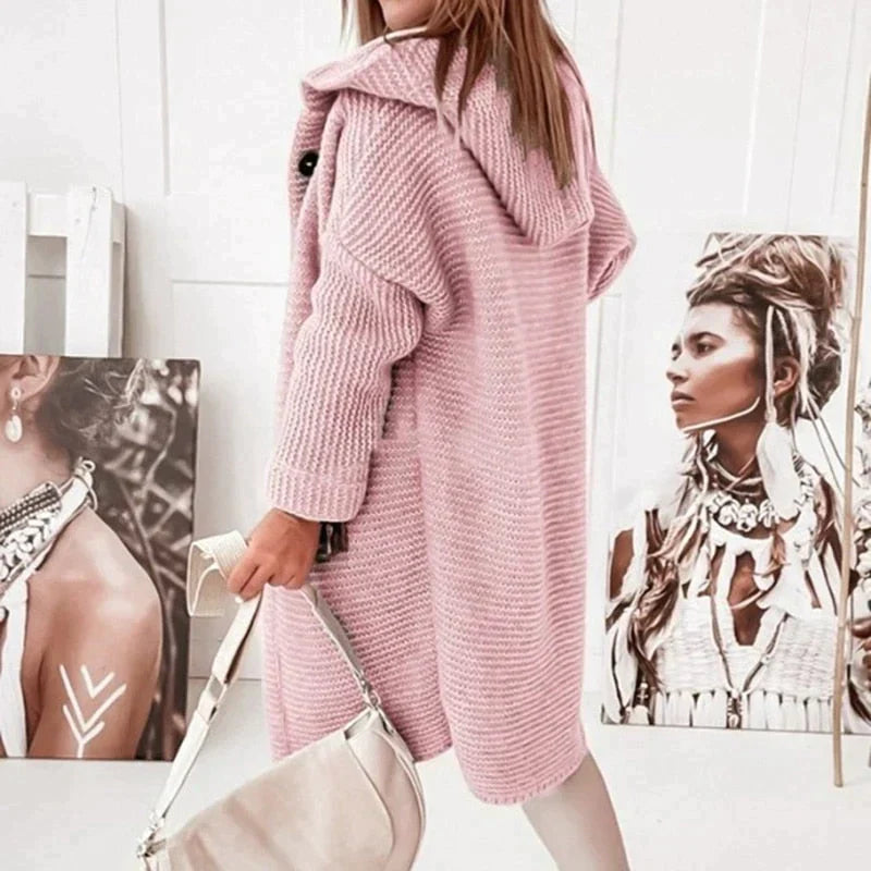 Seitenansicht einer Frau, die eine lange, rosa Strickjacke mit Kapuze trägt und eine Tasche hält