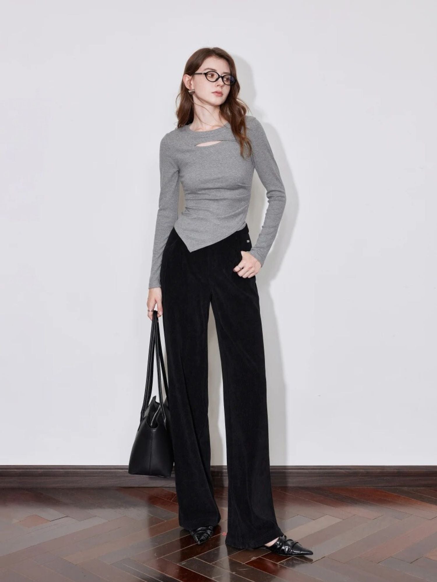 Model in black wide-leg trousers with grey ribbed top and black handbag.