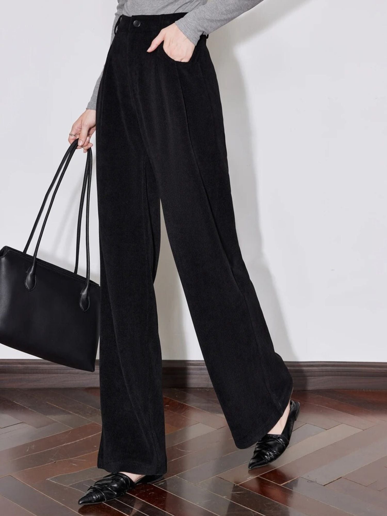 Side view of model walking in black pleated trousers and flat shoes.