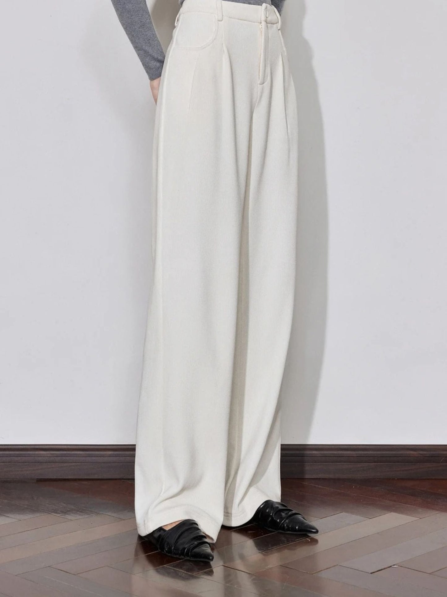 Side view of cream trousers with pleated front and loose fit.