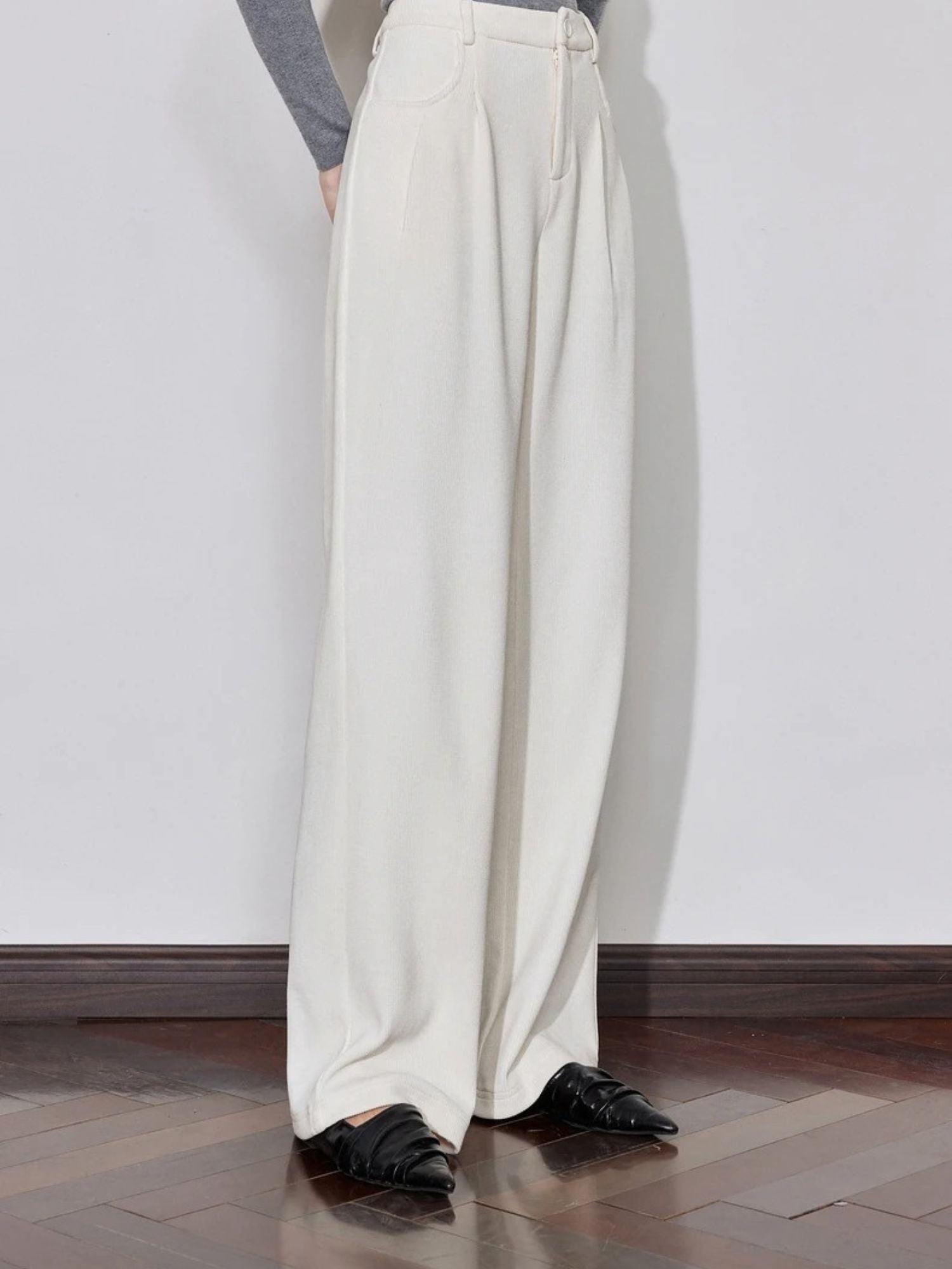 Side view of cream trousers with pleated front and loose fit.