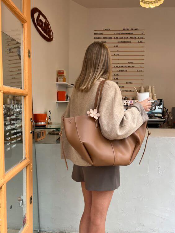 Eine frau mit einer braun ledertasche und einem kaffee steht an der cafétheke
